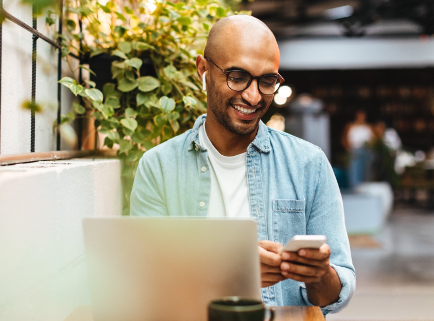 Image of a man using his cellphone while working on a laptop at a cafe table